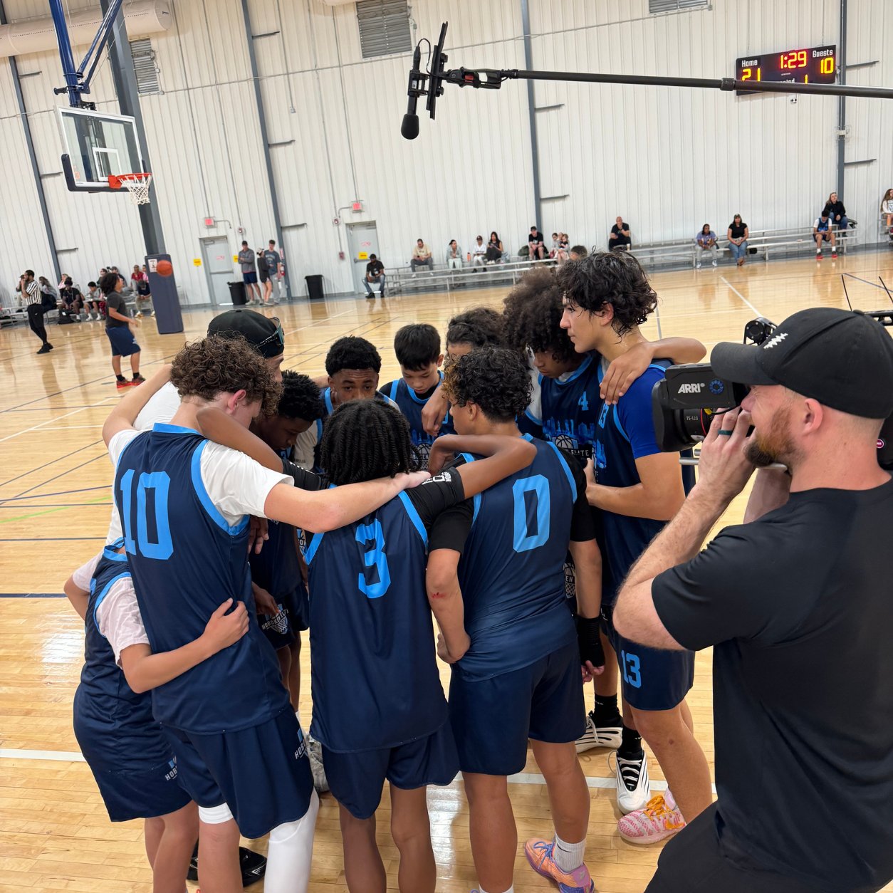 Youth basketball team huddled together mid-game as a Legacy Line Media crew member films courtside